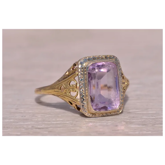 Gold ring with a purple gemstone on a light wooden surface