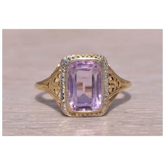 Gold ring with a purple gemstone on a light wooden surface