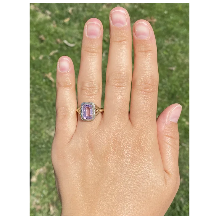 Hand wearing a ring with a purple gemstone against a grassy background