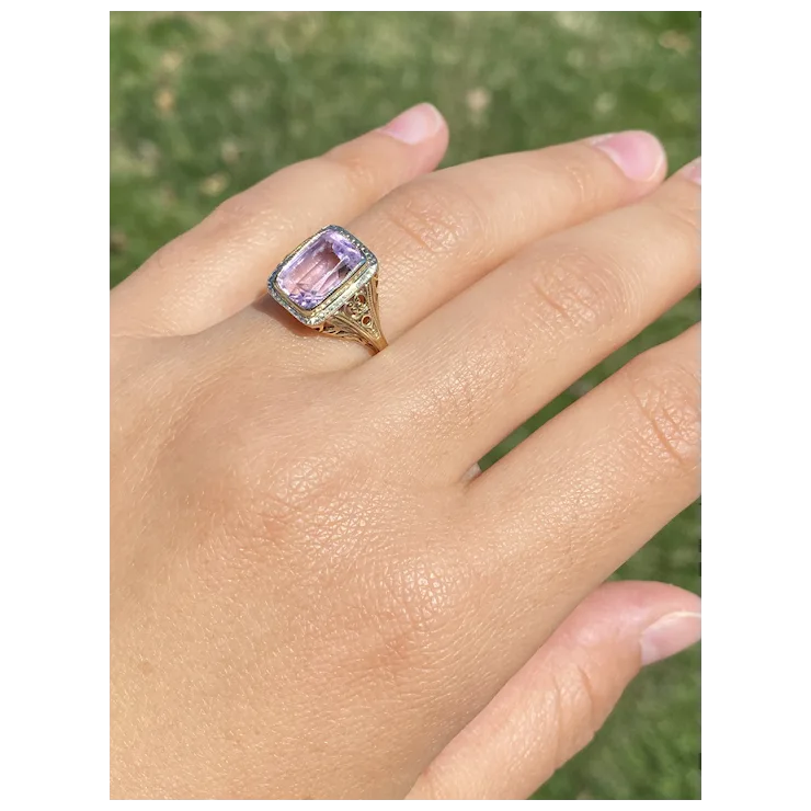 Hand wearing a ring with a pink gemstone against a blurred green background