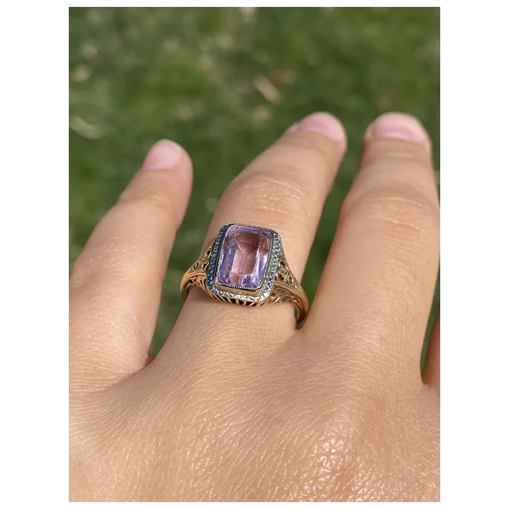 Ring with a purple gemstone on a finger against a blurred green background