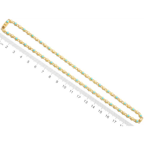 Gold chain with turquoise stones next to a ruler on a white background