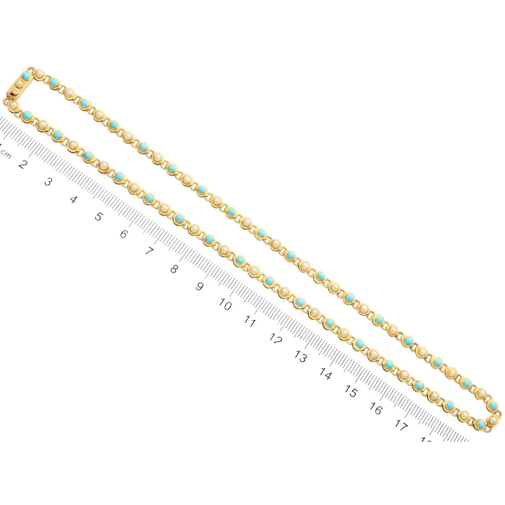 Gold chain with turquoise stones next to a ruler on a white background