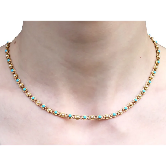 Gold necklace with turquoise stones on a plain background