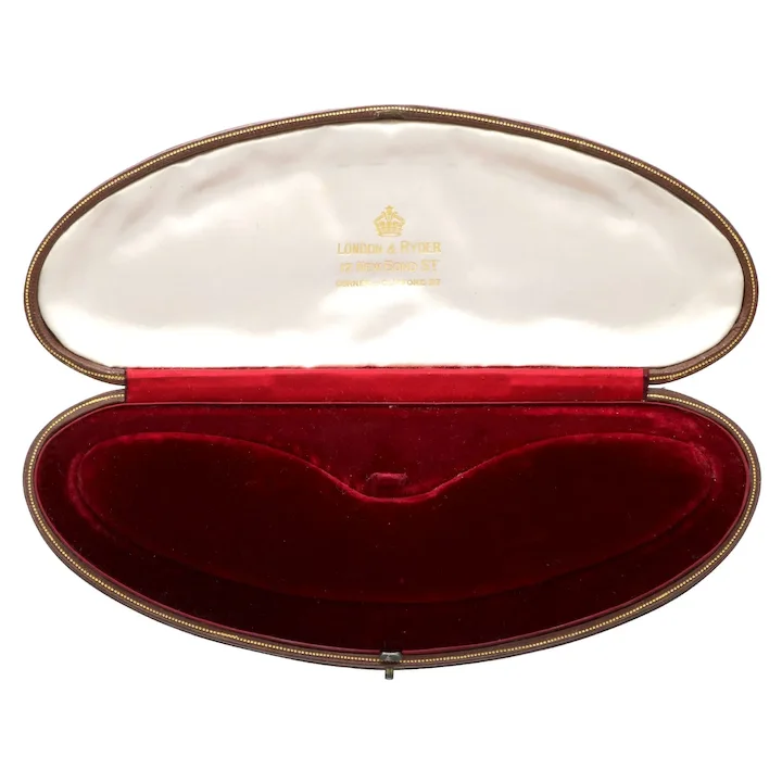 Oval jewelry box with red interior and gold exterior, featuring a brand logo.