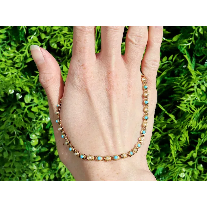 Hand wearing a beaded bracelet with turquoise stones against a green leafy background
