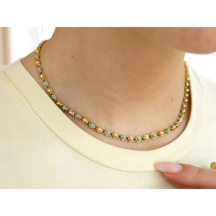Gold necklace with turquoise stones worn by a person on a white background