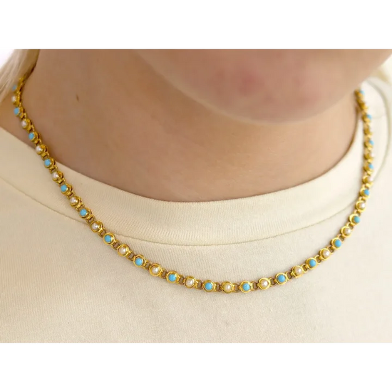 Gold necklace with blue stones worn by a person on a white background