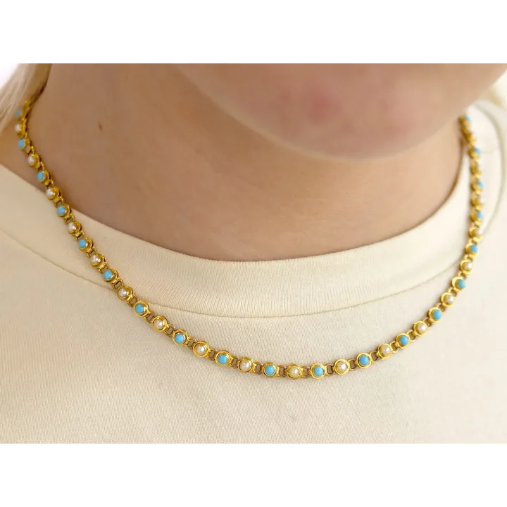 Gold necklace with blue stones worn by a person on a white background