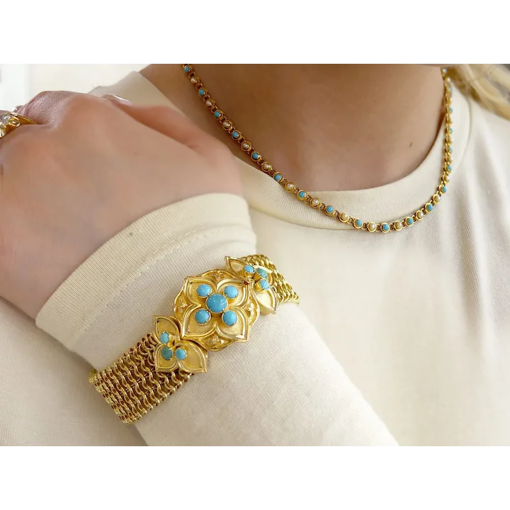 Gold bracelet with turquoise stones on a person wearing a white shirt.