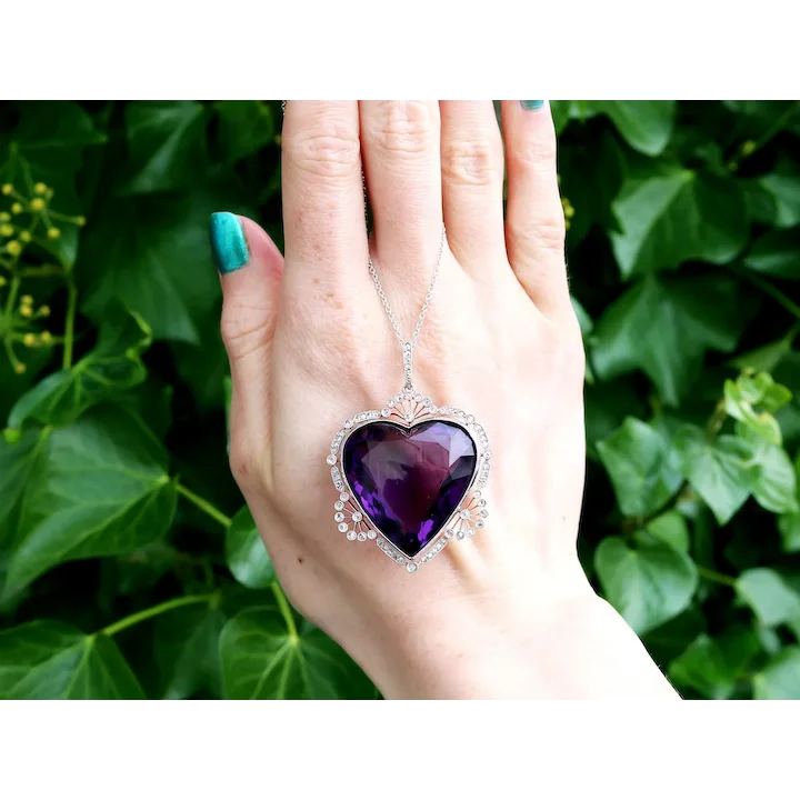 Hand holding a purple heart-shaped pendant against a green leafy background