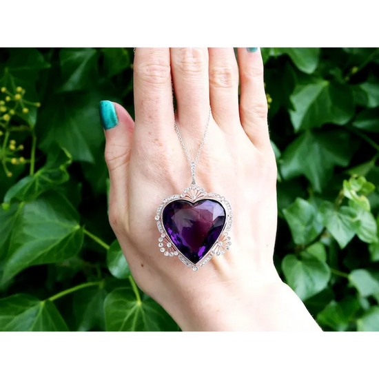 Hand holding a purple heart-shaped pendant against a green leafy background