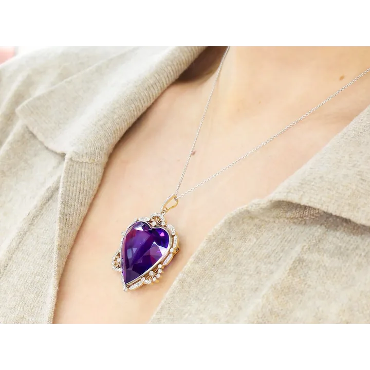 Purple heart-shaped pendant on a necklace worn by a person in a beige sweater.