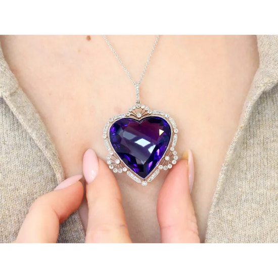 Heart-shaped purple gemstone necklace held by a hand