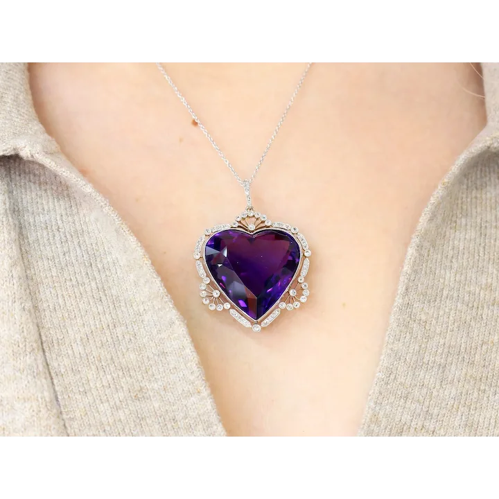 Necklace with a purple heart-shaped pendant on a person wearing a beige sweater.