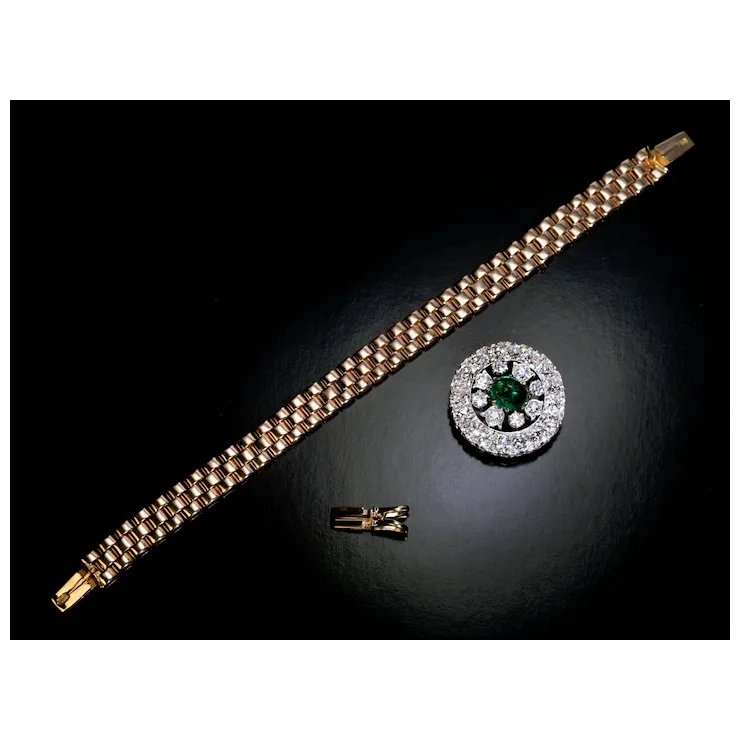 Gold bracelet and silver brooch with green gemstone on a dark surface