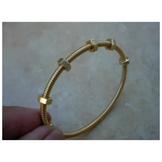 Gold bracelet with hexagonal links held by a hand on a beige background