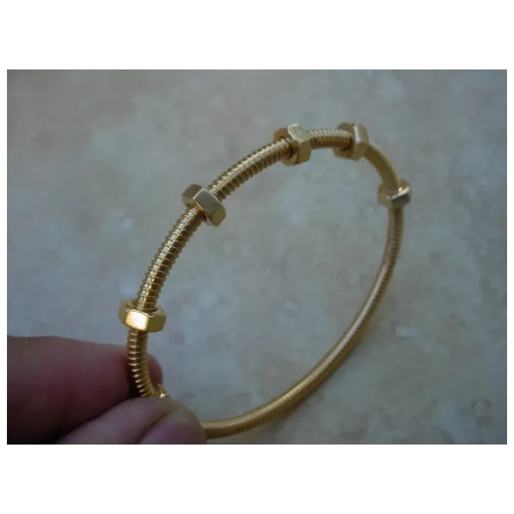Gold bracelet with hexagonal links held by a hand on a beige background
