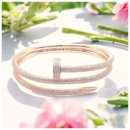 Rose gold bracelet on a white surface with blurred flowers in the background