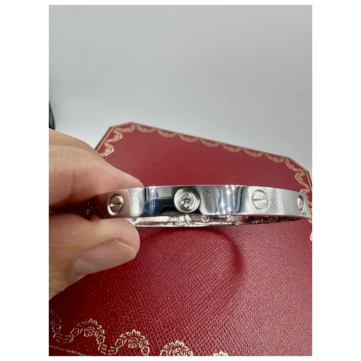 Silver bracelet with 'LOVE' engraving held by a hand on a red textured surface.