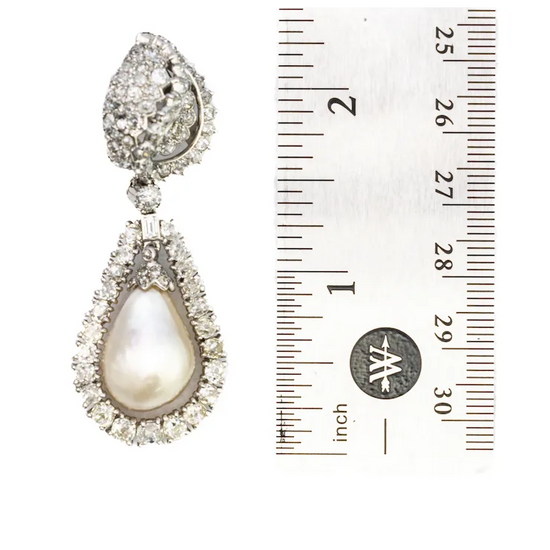 Teardrop-shaped pearl earring with diamond accents next to a ruler for scale on a white background