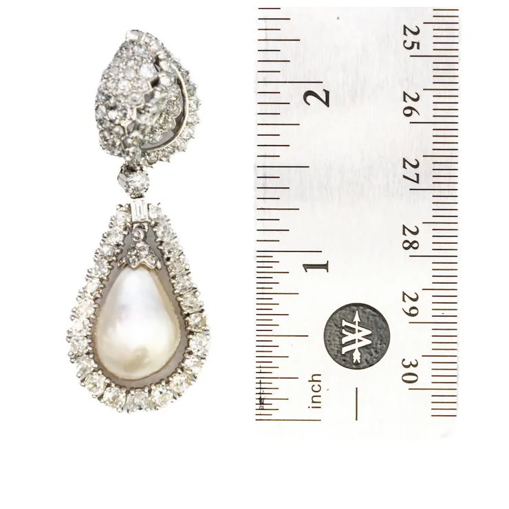 Teardrop-shaped pearl earring with diamond accents next to a ruler for scale on a white background
