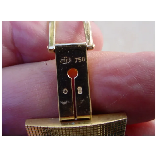 Gold bracelet with a clasp held between fingers on a light background