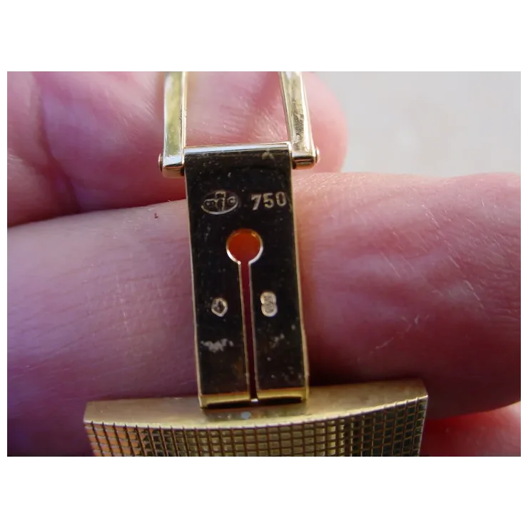 Gold bracelet with a clasp held between fingers on a light background