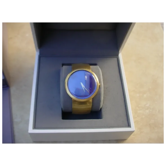 Gold watch with blue face in a box on a beige surface
