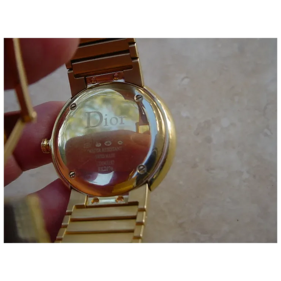 Gold watch with Dior branding on a neutral background