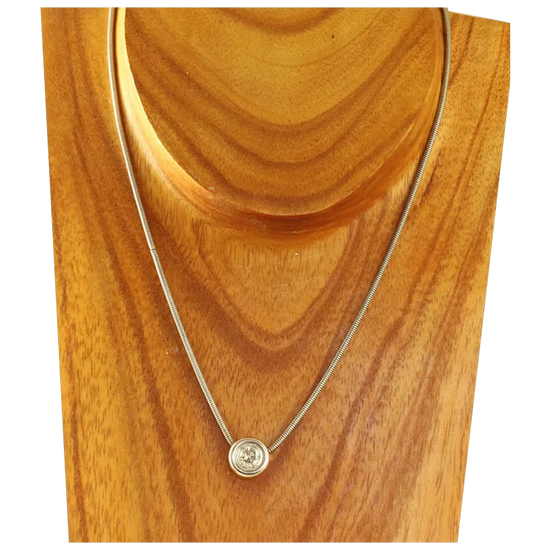 Gold necklace with a round pendant on a wooden stand