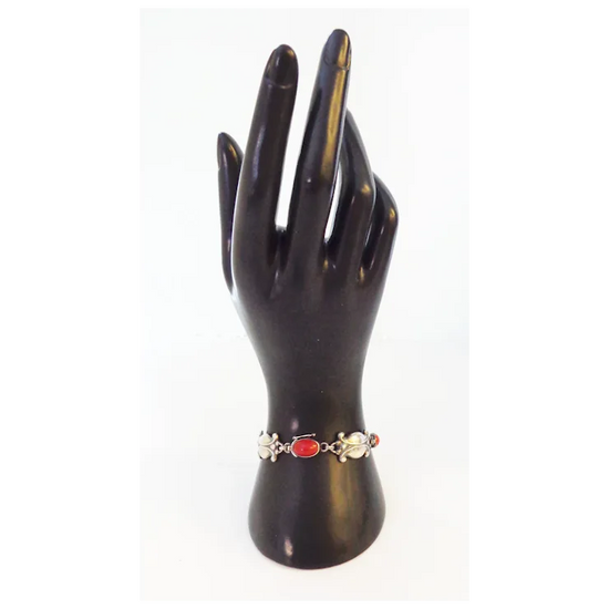Black mannequin hand holding a bracelet with a red gemstone on a white background