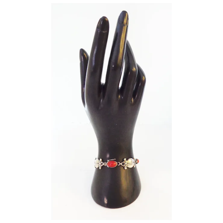 Black mannequin hand holding a bracelet with a red gemstone on a white background