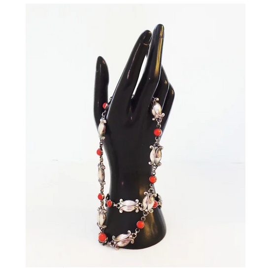 Necklace with red and silver beads on a black mannequin hand against a white background