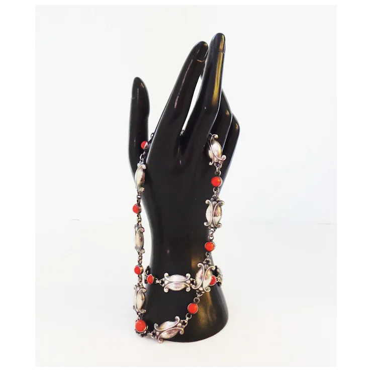 Necklace with red and silver beads on a black mannequin hand against a white background