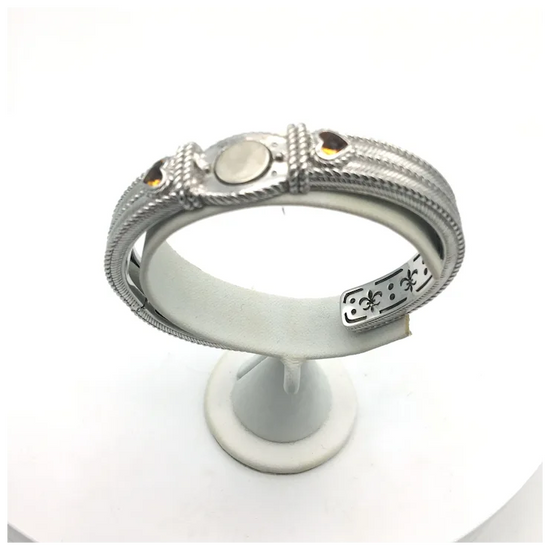 Silver bracelet with intricate designs on a white stand