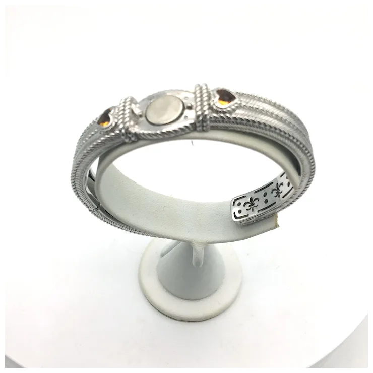 Silver bracelet with intricate designs on a white stand