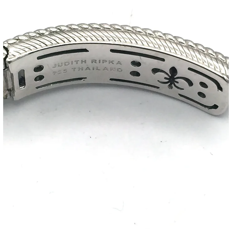 Close-up of a silver bracelet with 'Judith Ripka' engraving on a white background