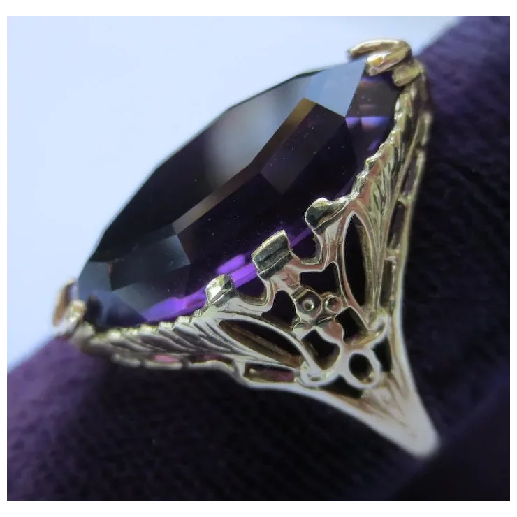 Gold ring with a large purple gemstone on a textured surface