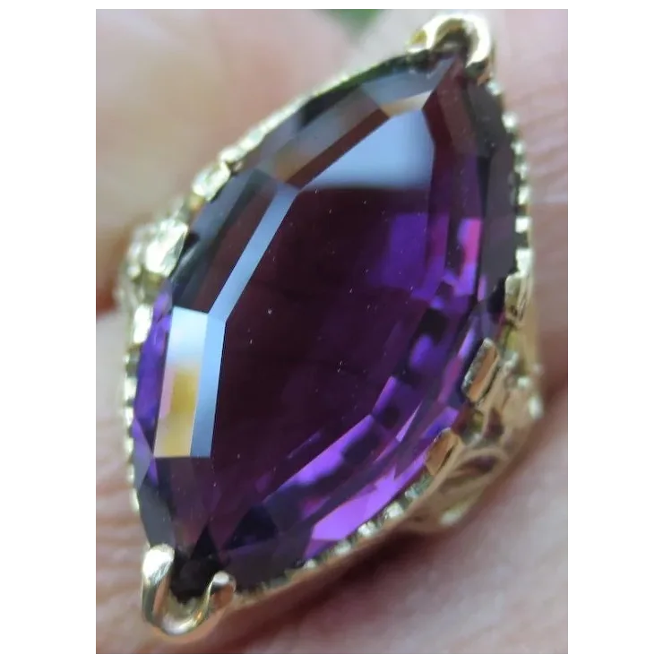 Gold ring with a large purple gemstone held between fingers.