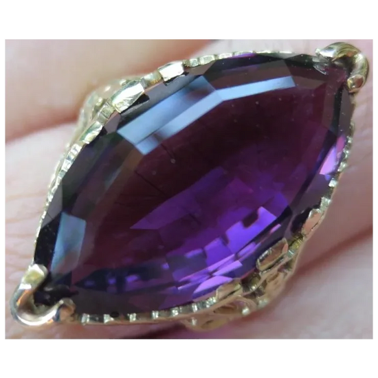 Purple gemstone in a gold setting held between fingers