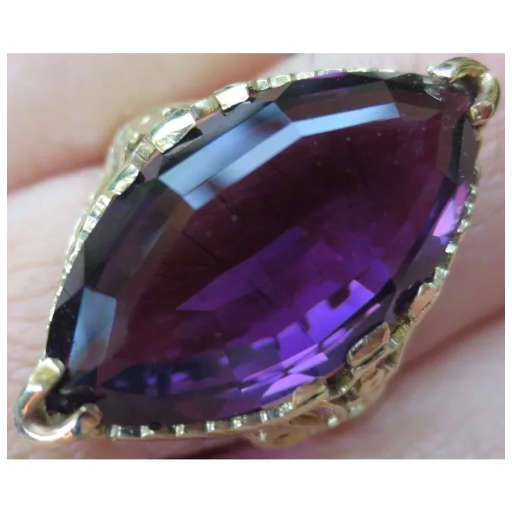 Purple gemstone in a gold setting held between fingers