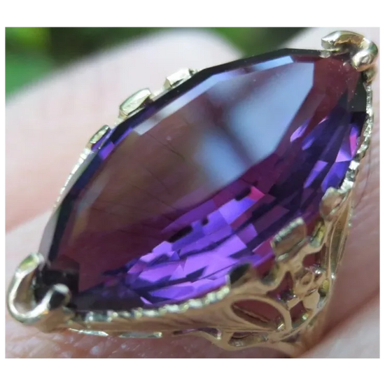 Gold ring with a large purple gemstone held in hand