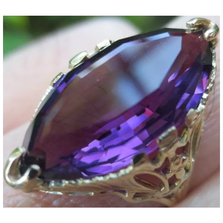 Gold ring with a large purple gemstone held in hand