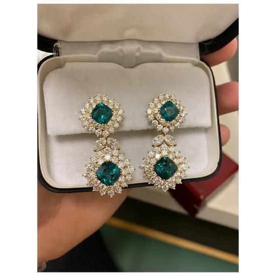 Pair of emerald green earrings with diamond-like stones in a jewelry box.