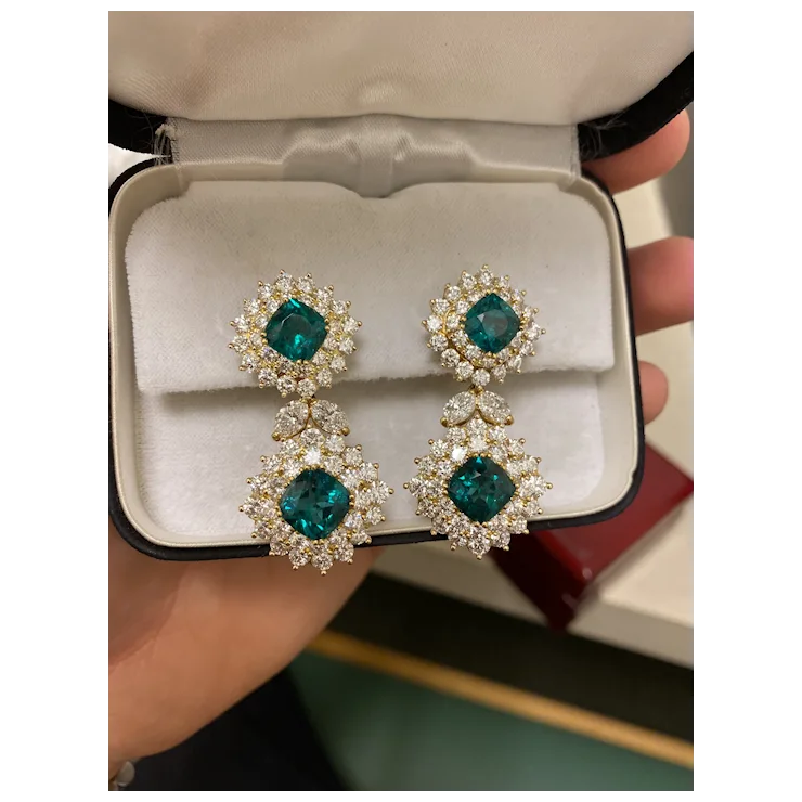 Pair of emerald green earrings with diamond-like stones in a jewelry box.