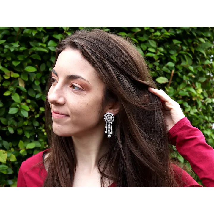 Woman with long brown hair and a red top against a green hedge background
