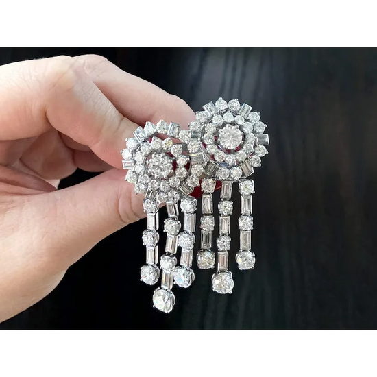 Diamond earrings held by a hand against a dark background