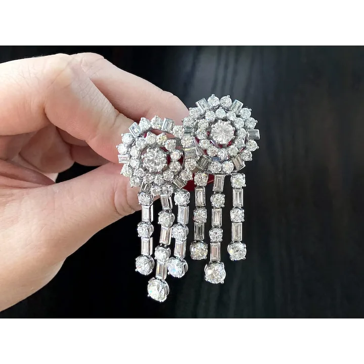 Diamond earrings held by a hand against a dark background