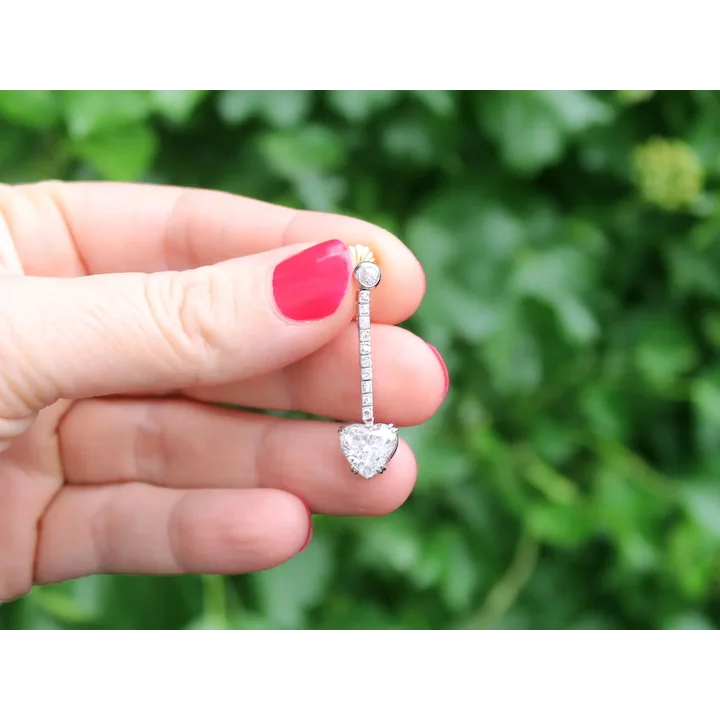 Heart-shaped diamond earring held between fingers with a blurred green background